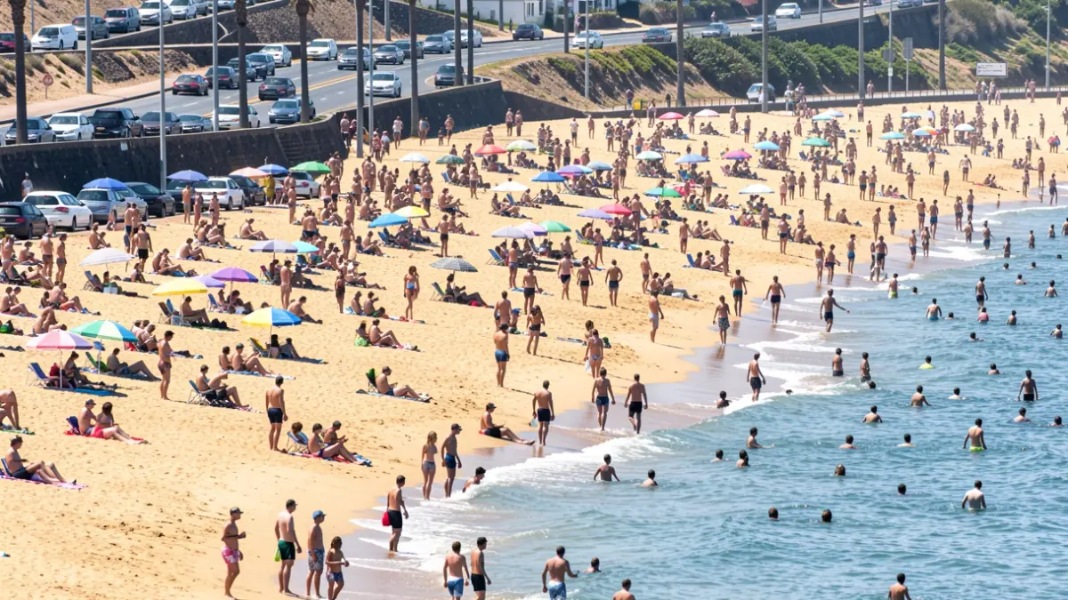 Imagen de la playa de Las Teresitas abarrotada de gente durante una ola de calor, con tráfico en la carretera de acceso.